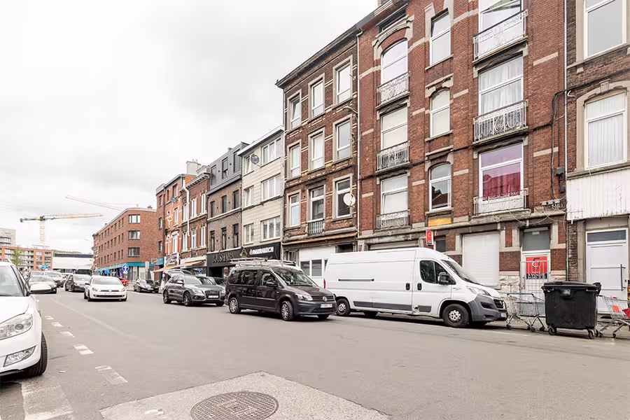 façade prise entre deux voitures, une poubelle et un panneau