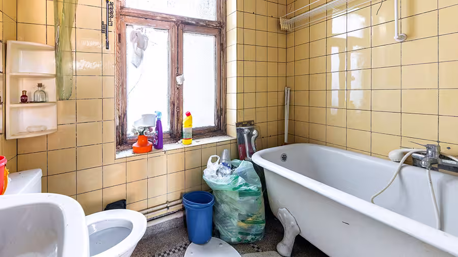 Petite salle de bains ancienne avec baignoire, carrelage jaune et objets du quotidien